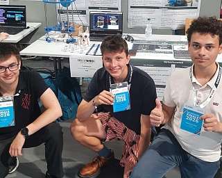 Die Schüler Karsten, Mateo und Lucas vom Team Curiositum der Hermann Lietz-Schule Spiekeroog präsentieren beim Deutschlandfinale der World Robot Olympiad 2026 in Trier ihre Teilnehmerausweise vor ihrem Wettbewerbsstand.