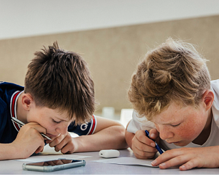 Zwei Schüler der Hermann Lietz-Schule arbeiten hoch konzentriert gemeinsam an einer Aufgabe. Ein Smartphone liegt ungenutzt auf dem Tisch.
