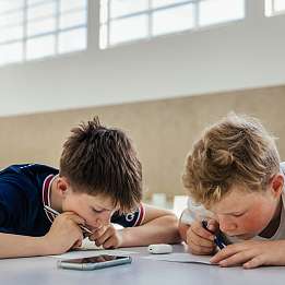 Zwei Schüler der Hermann Lietz-Schule arbeiten hoch konzentriert gemeinsam an einer Aufgabe. Ein Smartphone liegt ungenutzt auf dem Tisch.