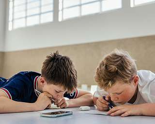 Zwei Schüler der Hermann Lietz-Schule arbeiten hoch konzentriert gemeinsam an einer Aufgabe. Ein Smartphone liegt ungenutzt auf dem Tisch.