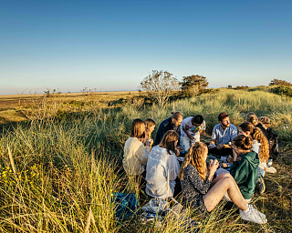 Schülerinnen und Schüler der Hermann Lietz-Schule sitzen gemeinsam in den Dünen auf Spiekeroog und verbringen Zeit in der Natur.